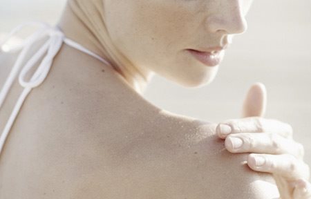 Nő krémmel keni be jobb vállát.